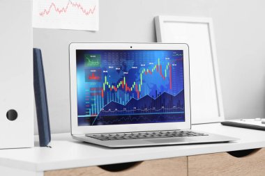 Tüccarın ofisindeki masanın üzerinde döviz kurlarının diyagramlarıyla dizüstü bilgisayar.