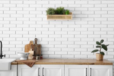 Mutfaktaki beyaz tuğla duvarın yanındaki tezgahlara teçhizat ve bitki koyun.