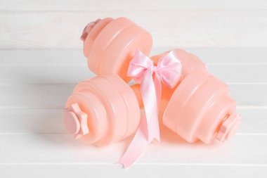 Beyaz ahşap arka planda fiyonklu pembe halterler.