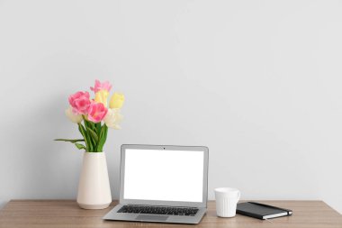 Modern dizüstü bilgisayarı ve beyaz duvarın yanında güzel çiçekleri olan şık çalışma alanı