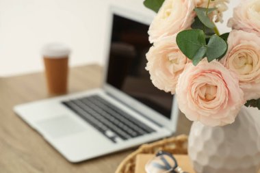 Modern dizüstü bilgisayarlı ahşap masa ve ev ofisinde güzel çiçekler, yakın plan.