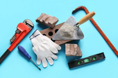 Mavi arka planda tuğla, eldiven ve inşaat araçları