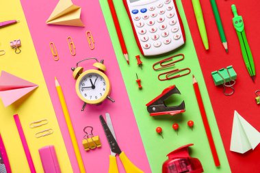 Alarmlı saat ve renkli arka planda kağıt uçaklar içeren okul kırtasiyesi