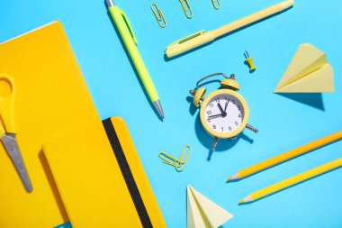 Saat, kağıt uçaklar ve mavi arka planda okul kırtasiyesiyle kompozisyon