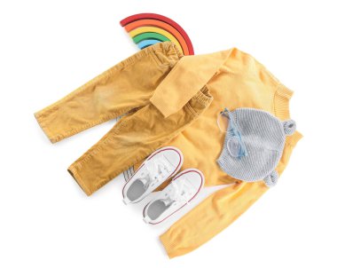 Beyaz arka planda şık çocuk kıyafetleri, gözlükler, ayakkabılar ve oyuncak gökkuşağı.