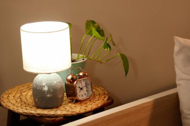 Parlak lambalı çalar saat ve yatak odasındaki masada bitki.