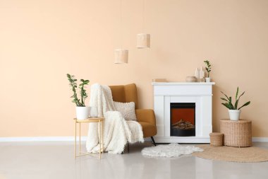 Odanın içindeki bej duvarın yanında şömine, masa ve koltuk.