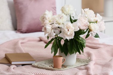 Kahve tepsisi, şakayık çiçekleri ve yatakta kitaplar.