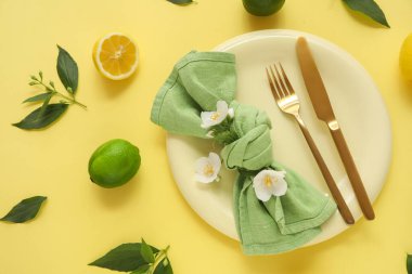 Tabağı, altın çatalı, turunçgilleri ve sarı arka planda çiçekleri olan güzel bir masa. Yakın plan.