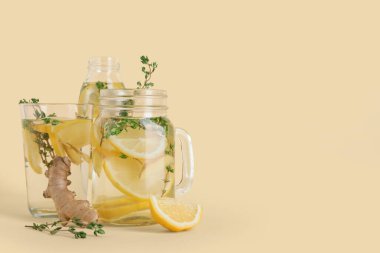 Mason kavanozu ve bir bardak taze limon karışımı zencefil ve kekik katılmış sarı arka planda.