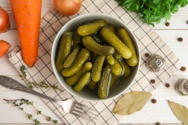 Lezzetli salatalık turşusu ve beyaz ahşap arka planda farklı malzemelerle dolu bir kase.