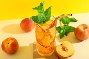 Bir bardak lezzetli buzlu çay, nane ve şeftali ile bej masanın üzerinde, sarı arka planda