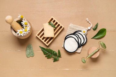 Çanta, yeniden kullanılabilir pamuk pedler, sabun çubuğu ve bej ahşap arka planda yeşil yapraklar.