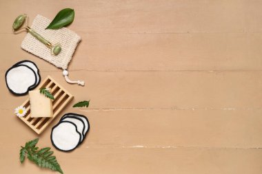 Çanta, yeniden kullanılabilir pamuk pedler, sabun çubuğu ve bej ahşap arka planda yüz masajı aracı