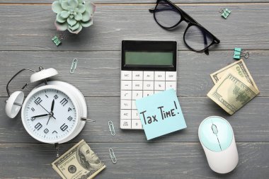 Hesap makineli çalar saat, bilgisayar faresi, gözlükler, para ve gri ahşap arka planda Vergi Zamanı