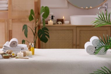 Plumeria çiçekli beyaz kanepe, temiz havlular ve banyonun içinde yanan mumlar.