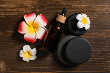 Taş, kozmetik ürün şişesi ve kahverengi ahşap arka planda tesisat çiçekleri olan güzel bir spa kompozisyonu, yakın plan.