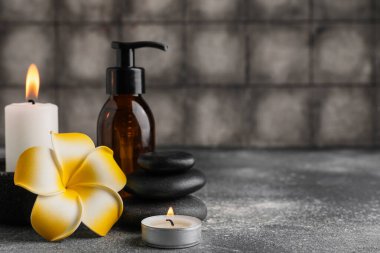 Güzel bir spa kompozisyonu, taşları, yanan mumları ve gri fayans duvarının yakınındaki gri grunge masasında bulunan plumeria çiçekleri.
