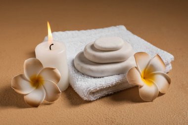 Plumeria çiçekleri, havlu, taşlar ve sarı grunge arka planda mum içeren spa kompozisyonu, yakın plan.