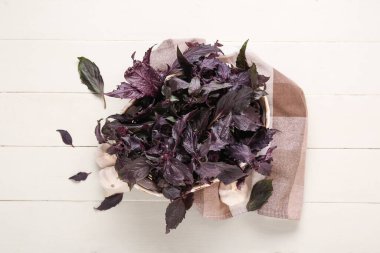 Beyaz ahşap arka planda taze mor fesleğen yapraklı sepet.