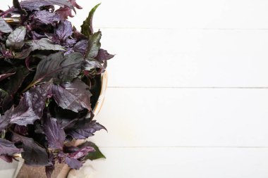Beyaz ahşap arka planda taze mor fesleğen yapraklı sepet.