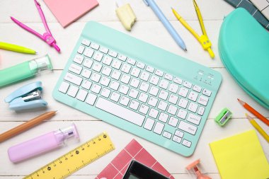 Beyaz ahşap arka planda bilgisayar klavyesi ve okul malzemeleri ile kompozisyon, yakın plan