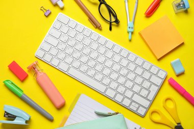 Modern bilgisayar klavyesine sahip kompozisyon ve sarı arkaplan üzerindeki farklı kırtasiye