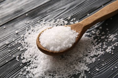 Koyu ahşap arka planda deniz tuzu olan kaşık, yakın plan.