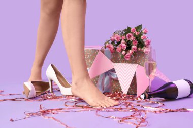 Leylak arkaplanındaki doğum günü partisinden sonra yüksek topuklu ayakkabı ve dekor giymiş bir kadın.