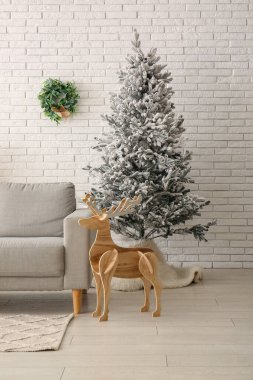 Tahta ren geyiği ve beyaz tuğla duvarın yanında rahat kanepesi olan güzel Noel ağacı.