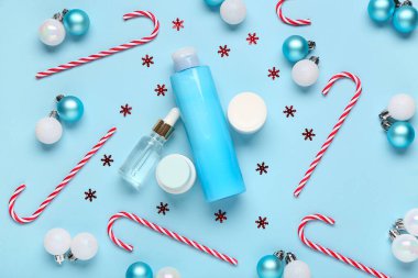 Noel baloları, konfetiler, baston şekerler, şişeler ve mavi arka planda kozmetik ürünleri kavanozları