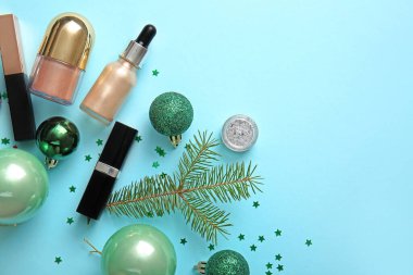Noel ağacı dallı farklı makyaj ürünleri ve mavi arka planda toplar