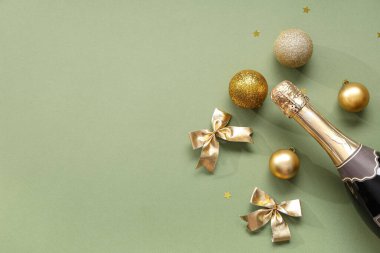 Bir şişe şampanyayla Noel topları ve yeşil arka planda fiyonklar