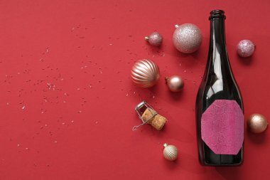 Bir şişe mantarlı şampanya ve kırmızı arka planda Noel topları.