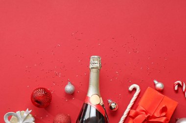 Kırmızı arka planda bir şişe şampanya, hediye kutuları ve şeker kamışları.