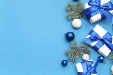 Hediye kutuları, köknar dalları ve mavi arka planda Noel süslemeleri olan şenlikli kompozisyon