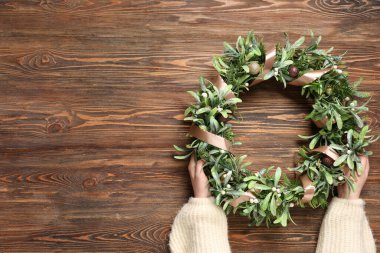 Kahverengi ahşap arka planda güzel ökseotu çelengi olan kadın elleri.