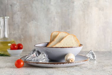 Tabakta lezzetli işlenmiş peynirli folyo ve gri arka planda bir kase ekmek dilimleri var.