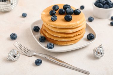 Yaban mersinli bir tabak tatlı krep ve beyaz arka planda Noel disko topları.
