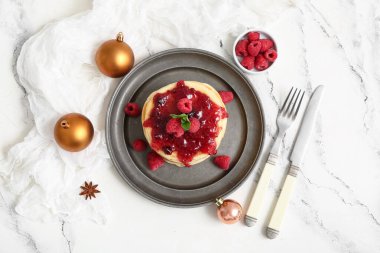 Ahududu reçelli bir tabak tatlı krep ve beyaz arka planda Noel topları.