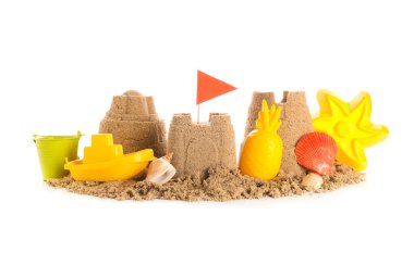 Plaj oyuncakları ve beyaz arka planda deniz kabukları olan kumdan bir kale.
