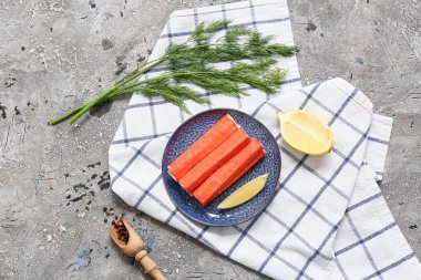 Lezzetli yengeç çubuklu tabak, gri arka planda limon ve dereotu kes.