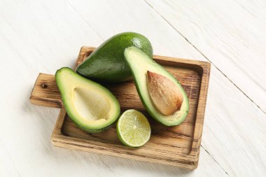 Taze olgun avokadolarla kesme tahtası ve beyaz ahşap arka planda yarım limon.
