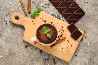 Nane yapraklı bir fincan sıcak çikolata ve gri grunge arka planda tarçın çubukları