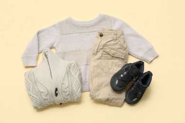 Bej arka planda şık çocuk kazakları, pantolonları ve botları.