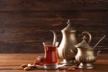 Çaydanlık, demlik, kurutulmuş hurma ve ahşap zemin üzerinde bademlerle bir bardak Türk çayı.