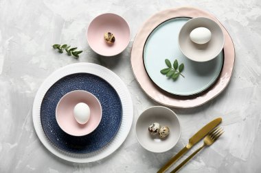 Paskalya yumurtaları ve gri arka planda taze yeşil yapraklarla farklı temiz tabaklar.