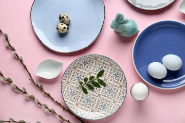 Different clean plates with Easter eggs, toy bunny and pussy willow branches on pink background
