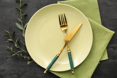 Siyah grunge arka planında çatal bıçak, peçete ve okaliptüs tabağı.