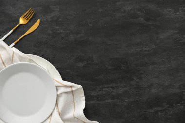 Siyah grunge arka planında çatal bıçak takımı ve peçeteyle tabak.